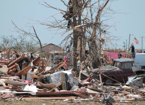 A tornado destroyed a town and a man raises a flag in the background.